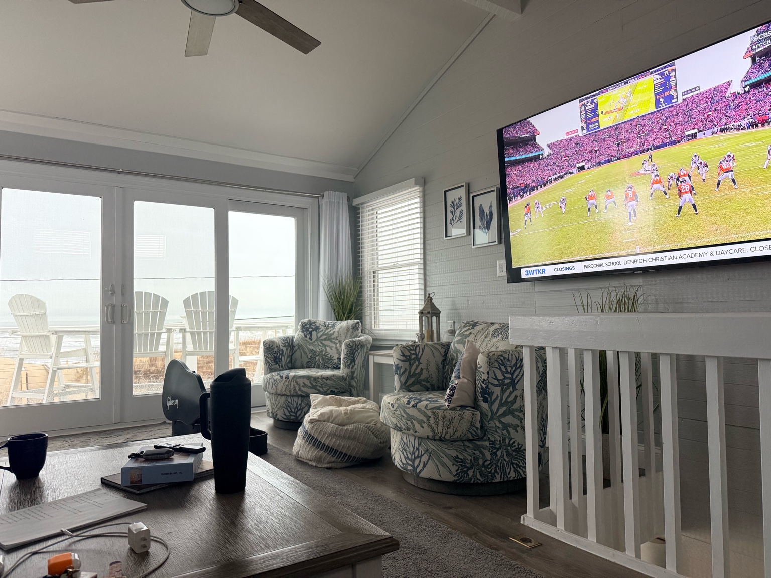Oceanfront living room with a large TV displaying a playoff game and ocean view from windows