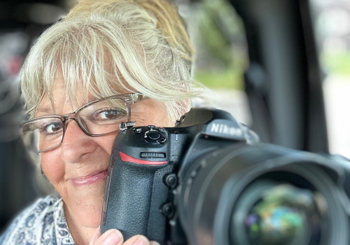 Dana holding her camera and smiling behind the lens