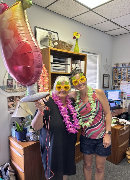 Dana and Leslie celebrating in the office with festive sunglasses and leis